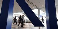 Hinter einem gewaltigen dreidimensionalen DeutscheBank-Logo sind verwischt Mitarbeiter und Kunden zu sehen