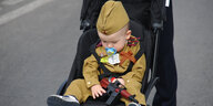 Baby in Militäruniform im Kinderwagen mit einer Spielzeugpistole