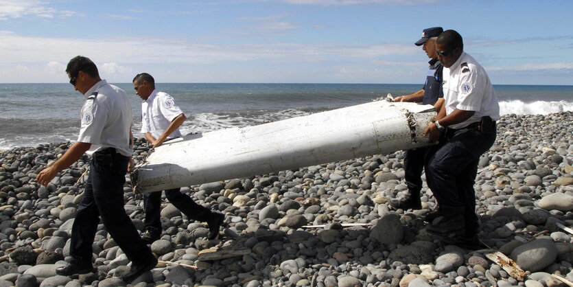 Vier Männer tragen ein Wrachteil am Strand von La Reunion