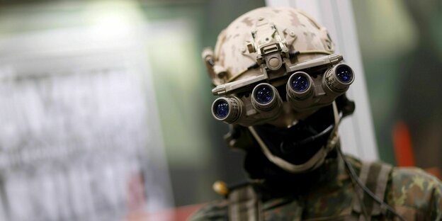 Ein Soldat mit Helm und Vermummung hat vier Ferngläser vor den Augen