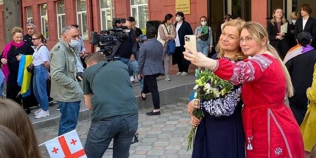 Eine Frau im roten Kleid macht ein selfie mit einer Frau mit Blumenstrauß