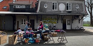 Vor einem alten Gebäude steht ein Tisch mit Kleidern. Darum herum stehen Leute.