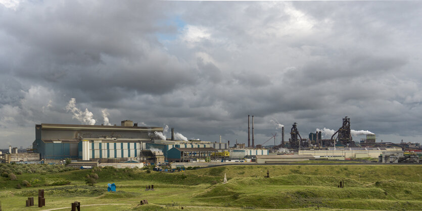 Rauchendes Stahlwerk , davor eine grüne Dünenlandschaft