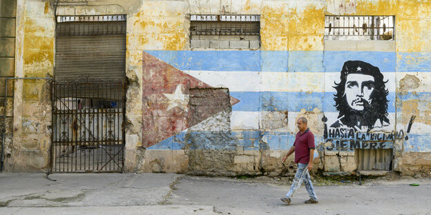 verblasstes Wandgemälde mit der kubanischen Fahne und Che Guevara, davor geht ein Mann vor dem verfallenen Haus