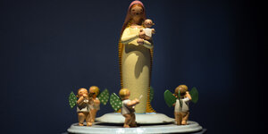 Eine hölzerne Marienfigur mit einem Baby auf dem Arm wird von kleinen Engeln umkreist.