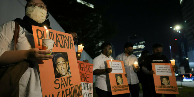 Activists hold orange signs with Nagaenthran's portrait on them