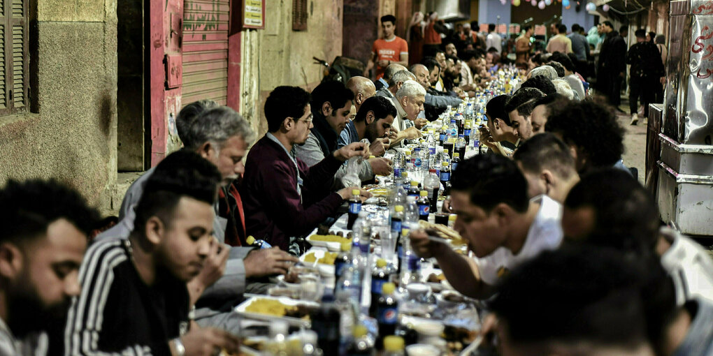 Männer sitzen in einer Gasse an gedeckten Tischen und essen