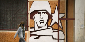 Soldatenkopf mit Stern, eine Wandmalerei, davor geht eine Frau