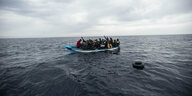 Menschen winken aus einem überfüllten Boot, ein Rettungsreifen liegt im Wasser