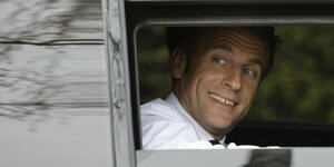 Der französische Staatspräsident Emmanuel Macron guckt gutgelaunt aus einem Autofenster