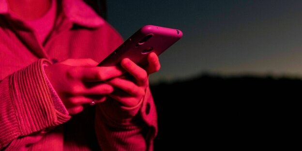 eine junge Frau hält ein Handy und ist von einem roten Licht angestrahllt