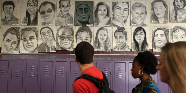 Menschen schauen auf Porträts der Ab­gän­ge­r:in­nen an einer Highschool in Boston