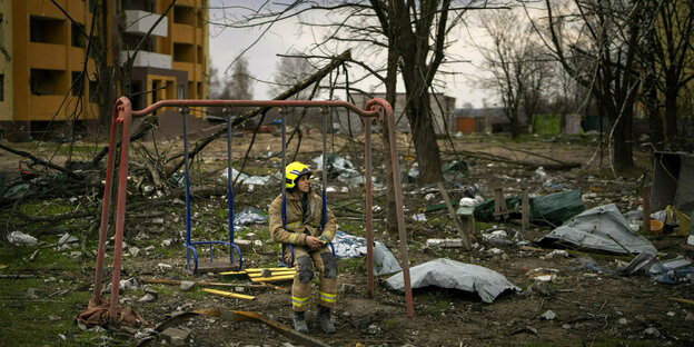 Ein Feuerwehrmann sitzt auf einer Schaukel neben einem von einer russischen Bombe zerstörten Gebäude