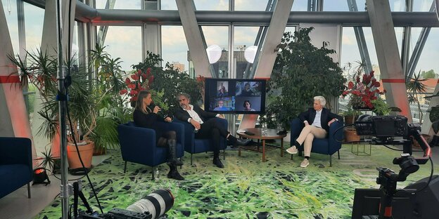 Jagoda Marinić, Deniz Yücel und Marie-Agnes Strack-Zimmermann auf Lounge-Stühlen zwischen Pflanzen im Panorama-Raum der taz, zwischen ihnen ein Bildschirm, weitere Personen sind zugeschaltet. Jagoda Marinić, Deniz Yücel und Marie-Agnes Strack-Zimmermann auf Lounge-Stühlen zwischen Pflanzen im Panorama-Raum der taz, zwischen ihnen ein Bildschirm, weitere Personen sind zugeschaltet.