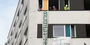 Transpis hängen an einer Häuserfassade, aus den Fenstern schauen Aktivistinnen