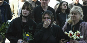 Trauernde Frauen mit Kopftuch und Blumen in der Hand