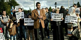 Eine Gruppe von Menschen, darunter Frauen mit Kopftüchern, hält Schilder in der Hand