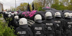 Aufgespannte Schirme, darunter Demonstrierende, davor Polizist:innen Aufgespannte Schirme, darunter Demonstrierende, davor Polizist:innen