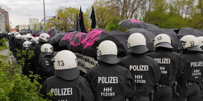 Aufgespannte Schirme, darunter Demonstrierende, davor Polizist:innen