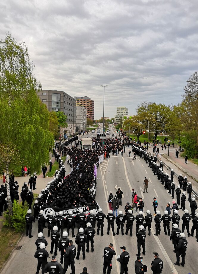 Blick von oben auf den Demonstrationszug. Vorne, links und rechts sind Polizeiketten