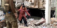 Begleitet von Bewaffneten klettert ein Kind über Trümmer