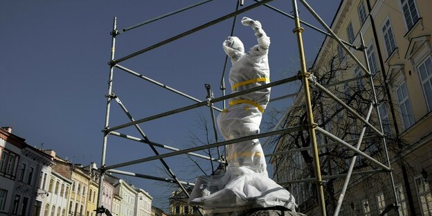 Eine Statue mit weißer Plastikfolie umwickelt und von einem Gerüst geschützt