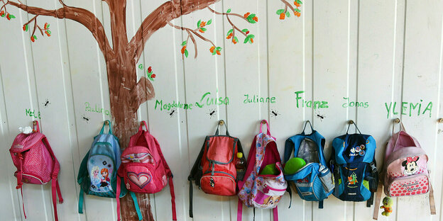 Kinderrucksäcke hängen an einer Wand, auf die ein baum gemalt ist
