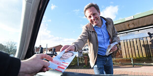 Thomas Losse-Müller reicht einen Flyer durch ein Autofenster