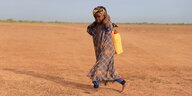 Ein Kind trägt einen Wasserkanister in einer kargen landschaft