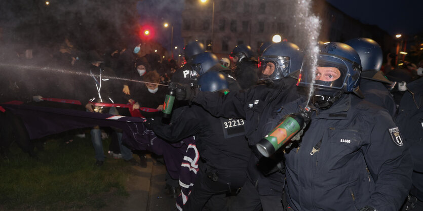 Ein Ploizist versprüht Pfefferspray am dunklen Oanienplatz, nicht nach vorne, sondern nach oben