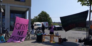 Person hält eine Rede zwischen pink-farbenem Banner mit der Aufschrift "Giffey not welcome" und dunklem Banner mit dem Giffey-Zitat "Wer sich wohnen nicht leisten kann, muss nach Rumänien zurück"