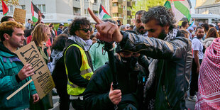 Szene einer Demo. Ein Mann in Lederjacke steht bedrohlich vor einem anderen. Er baut sich auf uns weist mit dem ausgestreckten Arm weg, so als sollte der anderen Mann fortgehen.