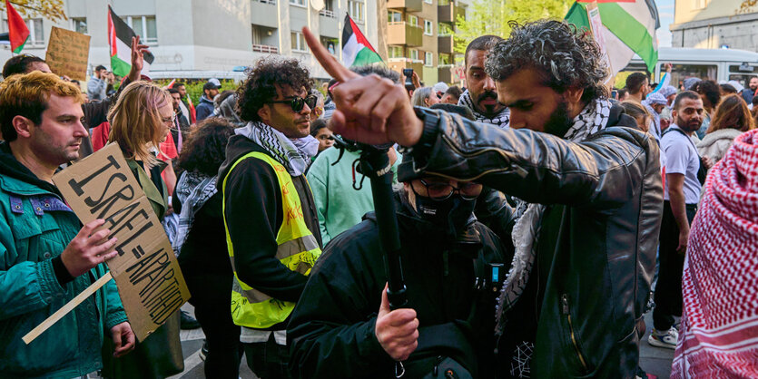 Szene einer Demo. Ein Mann in Lederjacke steht bedrohlich vor einem anderen. Er baut sich auf uns weist mit dem ausgestreckten Arm weg, so als sollte der anderen Mann fortgehen.