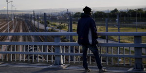 Ein Mann steht auf einer Brücke über Eisenbahngleisen