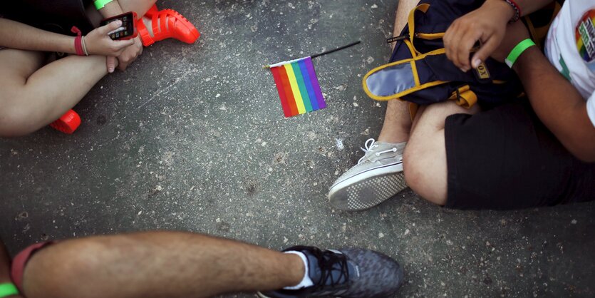 Auf der Erde sitzende Menschen mit Regenbogenfähnchen