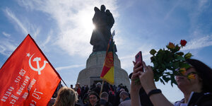 Zahlreiche Menschen stehen vor der Soldatenstatue am sowjetischen Ehrenmal, einer hält eine Flagge mit Hammer und Sichel