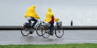 Zwei Radler in Regenmänteln auf einem Deich