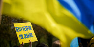 Eine blau-gelbe Fahne und ein blau-gelbes Plakat mit der Aufschrift "Heavy Weapon for Ukraine"