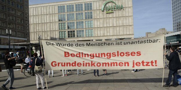 Ein Transparent mit Forderung nach einem Grundeinkommen steht auf dem Alexanderplatz