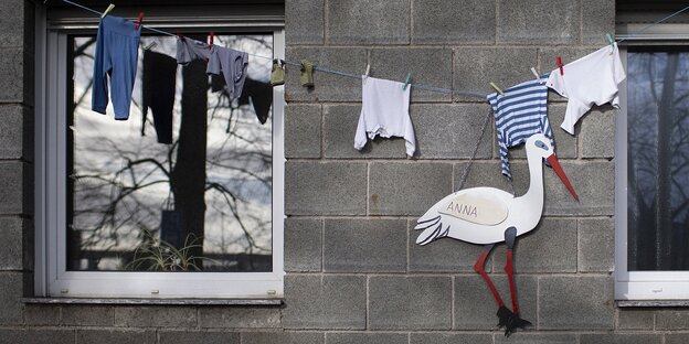 Eine Wäscheleine mit Babykleidung und das Bild eines Klapperstorchs an einer Hausfassade
