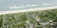 Ein Bild aus der Luft zeigt die Küste von Sylt. Oben ist das Meer zu sehen, dann der beige Strand und dann das Grüne Land, das mit roten gesprenkelt und von weißen Straßen durchzogen ist.
