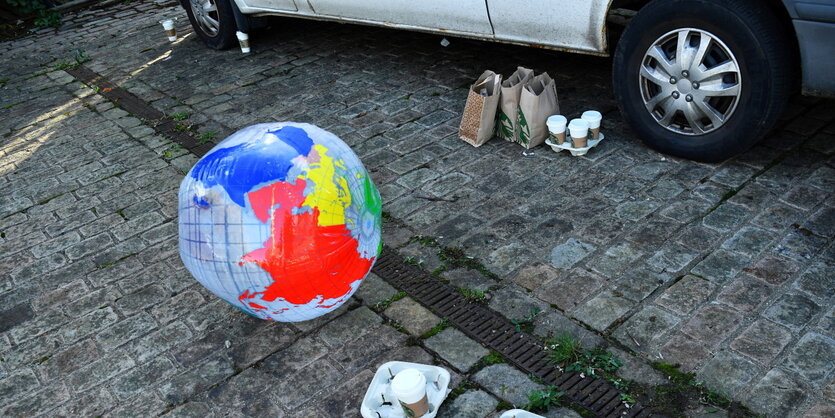 Ein uafblasbarere Globus liegt nebben Fastfood-Resten auf dem Asphalt