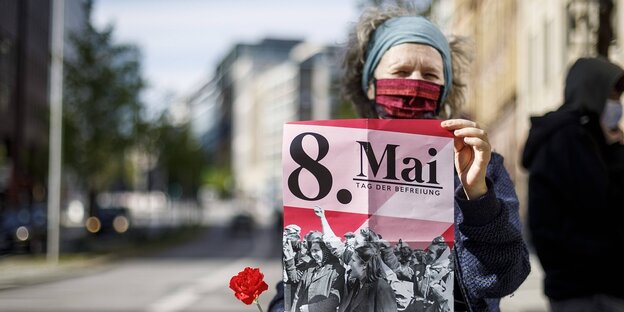 Eine Frau hält ein Plakat mit der Aufschrift "8. Mai - Tag der Befreiung"