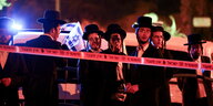 Hinter einer Polizeiabsperrung stehen Männer mit typisch jüdisch-orthodoxem Aussehen