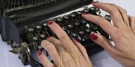 Zwei Hände mit roten Nägeln tippen auf einer Schreibmaschine