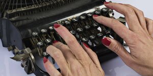Zwei Hände mit roten Nägeln tippen auf einer Schreibmaschine