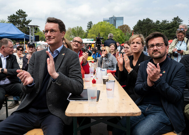 Auf Bierbänken sitzen Menschen und klatschen