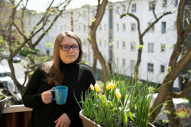 die Autorin steht auf ihrem bepflanzten Balkon mit einer Tasse in der Hand