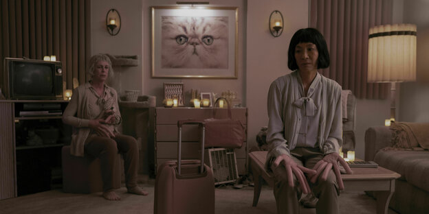 Jamie Lee Curtis und Michelle Yeoh sitzen mit Wurstfingern in einem Wohnzimmer.