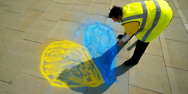 Ein Mann in gelber Warnweste malt ein blau-gelbes Herz auf die Strasse